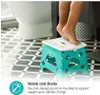 A child's legs are shown standing on a teal folding step stool in a bathroom. Náhled obrázku produktu