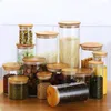 A collection of glass storage jars with bamboo lids filled with various dry goods like pasta, grains, beans, and coffee beans, arranged on a wooden surface. Produktbild-Vorschau