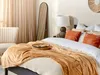 A bedroom scene with a bed, blanket, pillows, and a mirror. Podgląd zdjęcia produktu