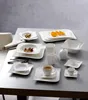 A collection of white ceramic tableware, including plates, bowls, cups, and a creamer, arranged on a table. Produktbild-Vorschau