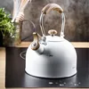 A white kettle with wooden accents sits on a black induction stovetop. Podgląd zdjęcia produktu
