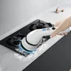 A hand is using an electric cleaning brush on a glass stovetop, with water splashing. Voir les images du produit