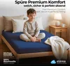 A young boy sits cross-legged on a navy blue fitted sheet on a bed, with pillows behind him and a white blanket draped over the side of the bed. A bedside table with a lamp and mug is visible. Náhled obrázku produktu