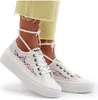 A pair of white lace-up sneakers with platform soles and ankle straps, worn by a person wearing light yellow cropped pants. Voir les images du produit