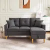 A dark gray sectional sofa with two pillows is shown in a well-lit living room with white paneled walls and a piece of abstract art on the wall. Podgląd zdjęcia produktu