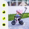 A young child sits in a pink tricycle with a canopy, outdoors on a paved path with grass in the background. There are four circular icons on the left side of the image. Produktbild-Vorschau