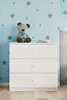 A white dresser with three drawers is shown in a child's room with blue walls decorated with gray stars. A teddy bear sits on top of the dresser. Náhled obrázku produktu