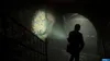 A person walks down a dark, graffiti-covered tunnel with a flashlight. Podgląd zdjęcia produktu