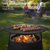 A griddle with food cooking on it over a fire, with people in the background. Produktbild-Vorschau