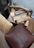 A pile of firewood in a rustic carrier next to a leather pouf and a woven cushion. Náhled obrázku produktu