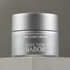 A silver jar of Babor The Cure Cream sits on a light gray surface against a darker gray background. Podgląd zdjęcia produktu