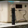 A black WUBEN LED flashlight is placed on a textured surface in front of a light-colored power station, with a charging cable connected. Produktbild-Vorschau