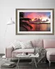 A living room scene with a pink sofa, a coffee table, and a framed picture of a sunset over the ocean hanging on the wall. Produktbild-Vorschau