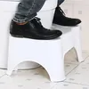 A person's feet wearing black shoes are standing on two white plastic steps next to a toilet. Podgląd zdjęcia produktu