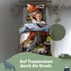 A young boy is sleeping in a bed with dinosaur-themed bedding. The bedding features images of dinosaurs and volcanoes. Produktbild-Vorschau
