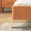 A close-up view of a wooden bed frame with a gold metal leg, resting on a rug. Voir les images du produit