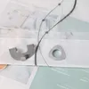 A close-up view of two metal accessories for a curtain or blind, placed on a fabric with a printed pattern. Produktbild-Vorschau