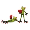 Two decorative frog figurines, each holding a red heart, are displayed against a white background. Produktbild-Vorschau