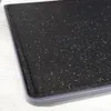 A close-up view of a black speckled cutting board with a gray edge, placed on a light-colored surface. Náhľad obrázku produktu