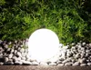 A glowing garden sphere sits among rocks in front of a green bush at night. Produktbild-Vorschau