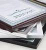 A close-up, angled view of several stacked picture frames, with the top frame displaying a certificate with German text. Produktbild-Vorschau