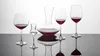 A collection of crystal glassware, including a decanter and several wine glasses, filled with red wine, displayed on a reflective surface against a white background. Náhled obrázku produktu