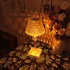 A crystal table lamp is placed on a patterned tablecloth next to a vase of flowers, casting intricate light patterns on the wall and table. Náhled obrázku produktu