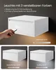 A white floating nightstand with a drawer is shown, with a hand holding a remote control pointing at it. The image also displays three different lighting effects: warm, natural, and cool light. Produktbild-Vorschau