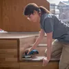 A woman is sanding wooden stairs with a power tool. Anteprima dell’immagine prodotto