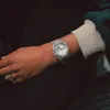 A close-up shot of a person's wrist wearing a silver watch and a ring. Produktbild-Vorschau