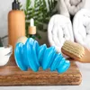 A blue massage tool is placed on a wooden board, with bathroom accessories like towels, a dispenser, and a brush in the background. Náhľad obrázku produktu