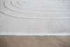 A close-up view of a cream-colored rug with a raised arched pattern, placed on a wooden floor. Produktbild-Vorschau