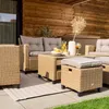 A polyrattan lounge set with a double sofa, two armchairs, two ottomans, and a coffee table is arranged on a patio with a wooden wall background. Produktbild-Vorschau