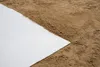 A close-up view of a white drainage fleece laid on top of brown soil. Produktbild-Vorschau