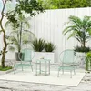 A green metal bistro set with two chairs and a table is placed on a light-colored rug on a wooden patio, surrounded by lush green plants and a white wooden fence. Podgląd zdjęcia produktu