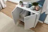 A white bathroom vanity cabinet with two doors, one open, revealing rolled towels inside. The cabinet is positioned next to a sink and a blue wall. Náhľad obrázku produktu