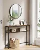 A narrow console table with two shelves is placed in a hallway, decorated with a mirror, framed pictures, a radio, books, and a woven basket. Produktbild-Vorschau