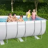 A family is enjoying themselves in a rectangular above-ground swimming pool on a sunny day, with lush green grass and trees in the background. Produktbild-Vorschau