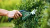 A hand is using a Bosch hedge trimmer to trim a green bush. Anteprima dell’immagine prodotto