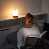 A young woman is reading a book in bed, illuminated by a bedside lamp. Produktbild-Vorschau