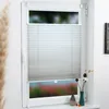 A window with white pleated blinds and decorative items on the windowsill. Produktbild-Vorschau