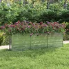 A galvanized steel raised garden bed filled with colorful flowers, set in a grassy garden with lush green bushes in the background. Produktbild-Vorschau