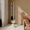 A modern oval floor mirror with a beige base is placed in a room next to a brown leather sofa and sheer curtains. Produktbild-Vorschau