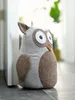 A stuffed owl doorstop is placed on a floor next to a white door frame. The background is blurred, showing greenery and light. Anteprima dell’immagine prodotto