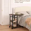 A C-shaped coffee table with shelves next to a bed. Produktbild-Vorschau