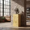A decorative pedestal with a mechanical sculpture on top, placed in a loft-style living room with exposed brick walls and large windows. Voir les images du produit