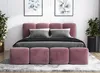 A pink upholstered bed with gray bedding and pillows, set against a white wall with two framed botanical prints and potted plants on either side. Produktbild-Vorschau