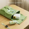 A green bag with a cartoon avocado design, containing a mini projector and other accessories, placed on a wooden table. Náhled obrázku produktu