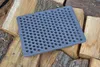 A gray metal grate with many holes rests on a pile of chopped firewood. Produktbild-Vorschau