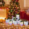 A Christmas tree decorated with ornaments and lights, surrounded by illuminated gift boxes on the floor, with a fireplace and candles in the background. Anteprima dell’immagine prodotto